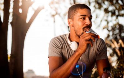 iStock-1053860752 African-American male with headphones eating chocolate candy bar while resting from outdoor exercise.