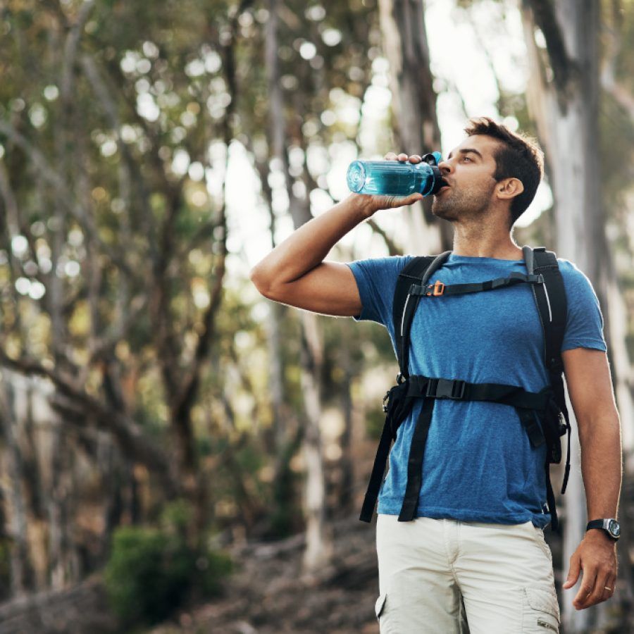 Cropped shot of a carefree young man drinking water from a bottle while going for a hike up a mountain